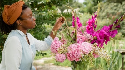 Quilenthia touching stem of floral arrangement in vase. Vase has link Hydrangeas, white Crape myrtle, magenta gladiolus 